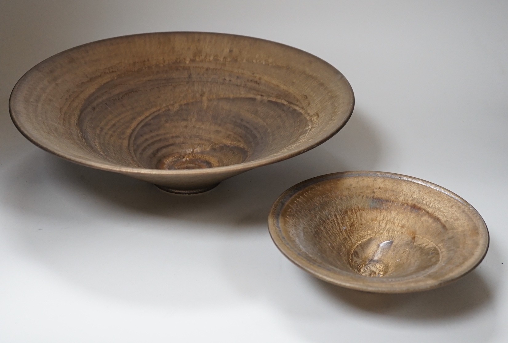 Huw Powell Roberts - two white earthenware open dishes covered in mottled bronze glaze with gold spiral decoration, incised HPR mark, 36.5cms and 19.5cms diameter